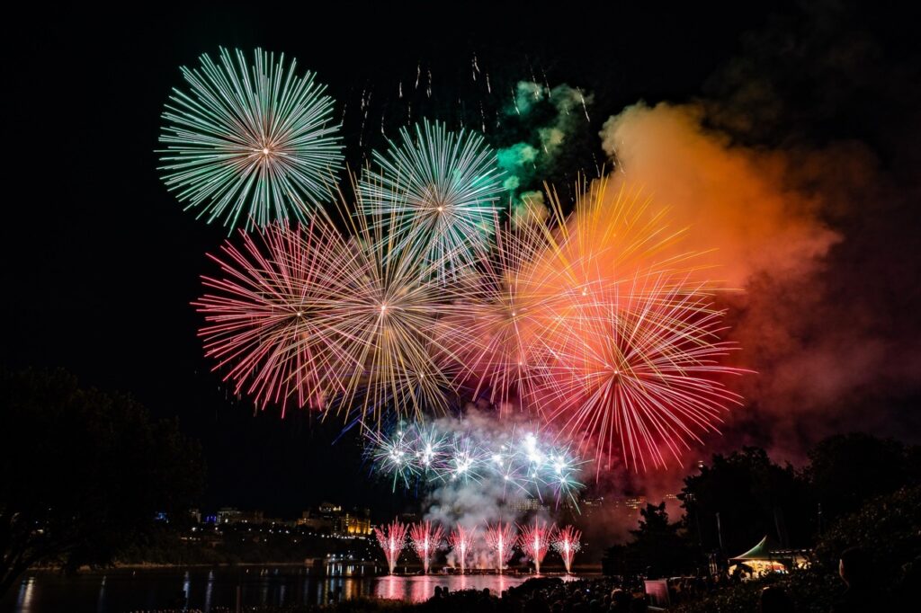 Plusieurs feux d’artifice, orange, rose et vert, vu du site des Grands Feux.