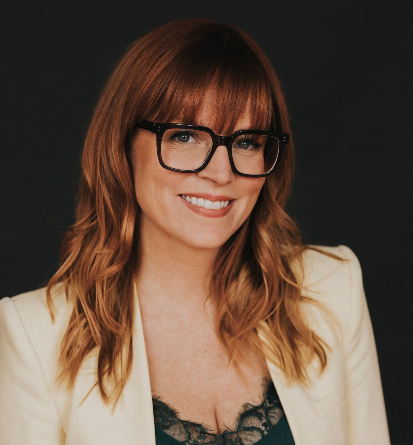 Portrait de Julie Moffatt qui sourit avec un veston blanc et des lunettes noires.