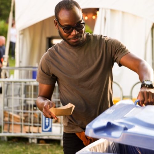 Homme portant des lunettes de soleil jetant son contenant en carton au recyclage.