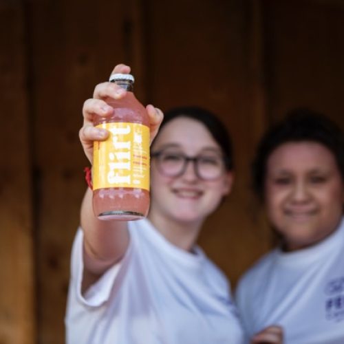 Deux personnes qui tiennent une bouteille orange de la marque « flirt ».